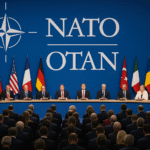 NATO leaders seated at a long table with national flags and NATO logo in the background during an official summit.